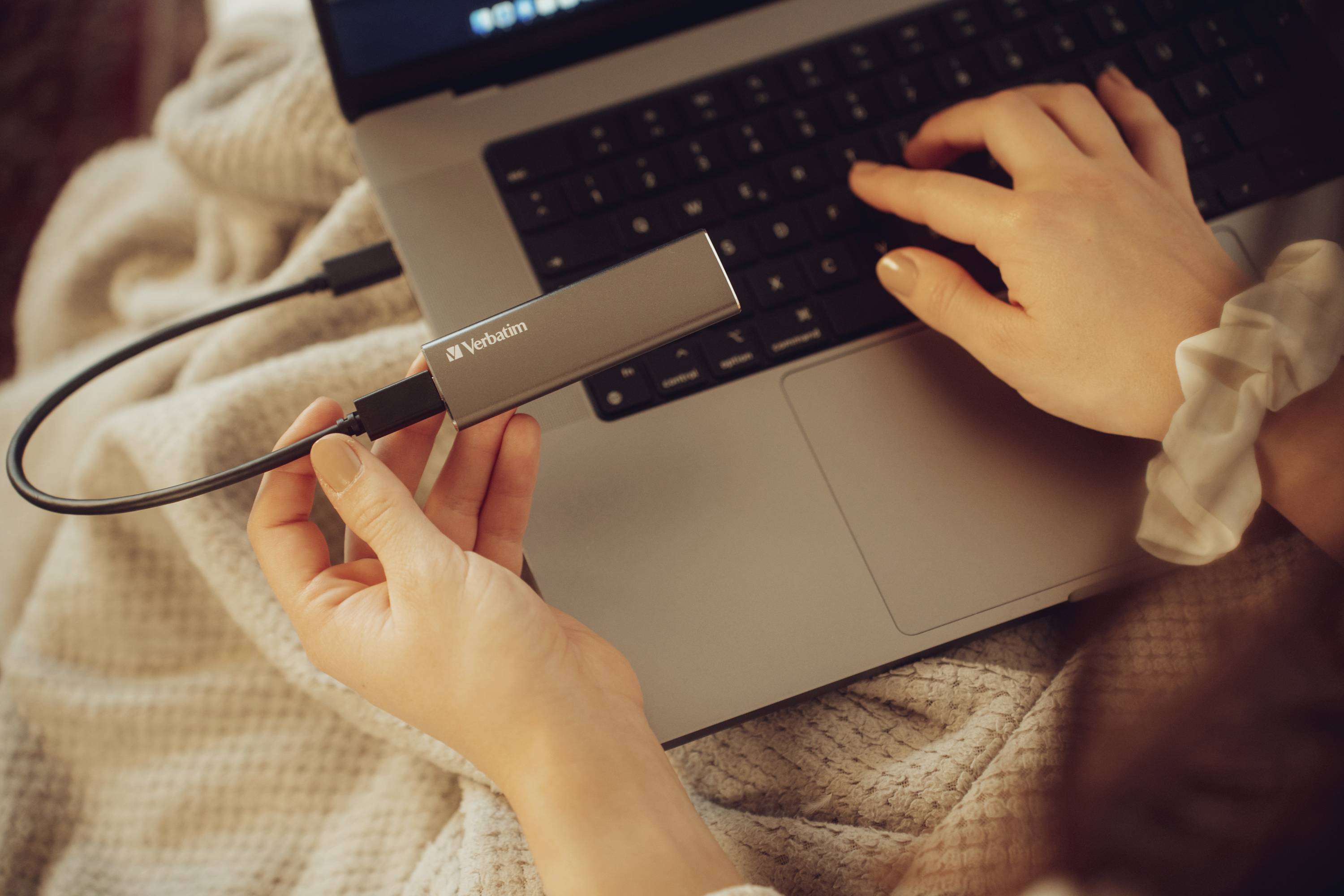Une personne utilise un ordinateur portable et tient un périphérique de stockage externe. Il est en cours de branchement alors que l'autre main repose sur le clavier.
