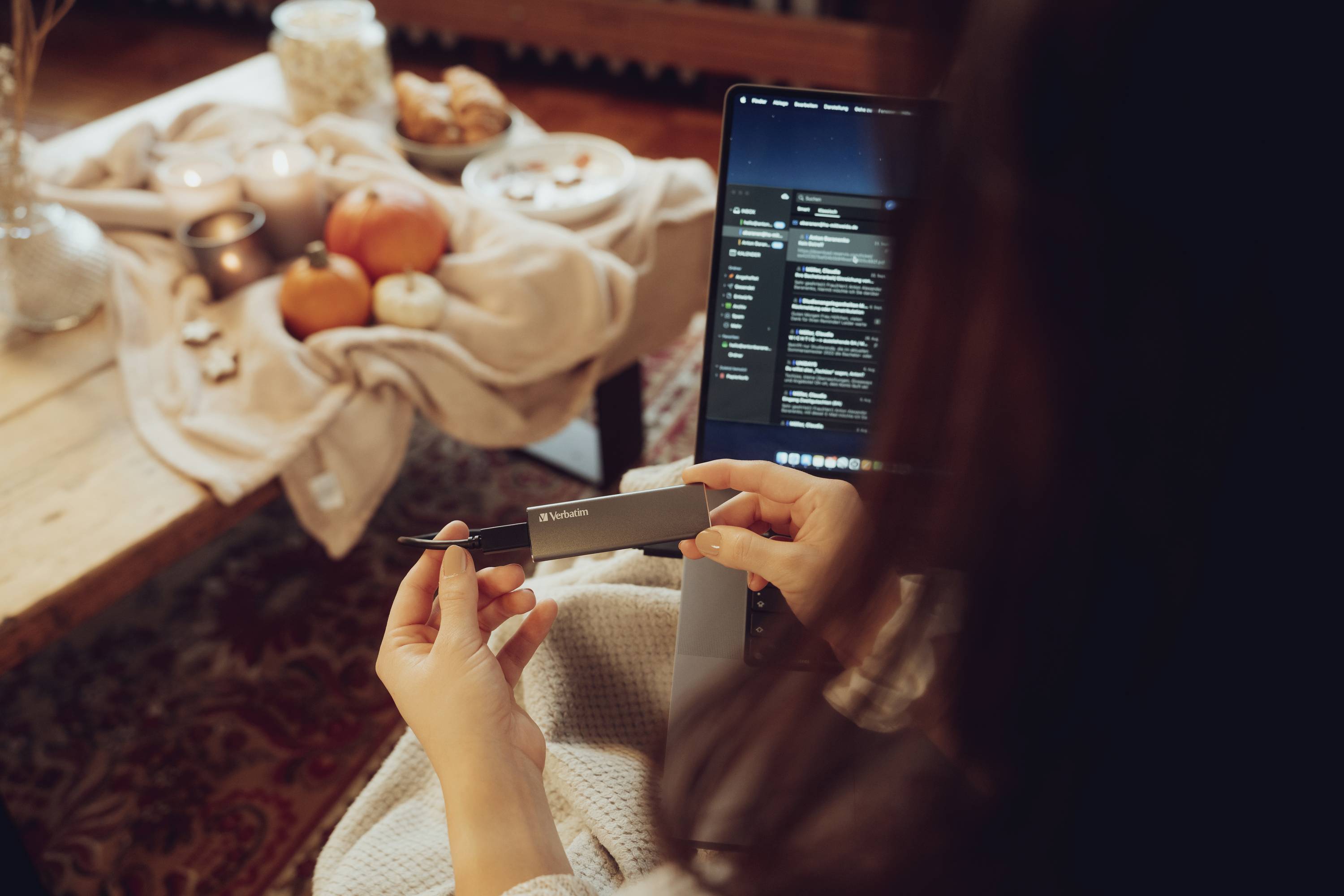 Une personne est assise à table, tenant un appareil électronique. L'écran de l'ordinateur portable affiche la boîte de réception des e-mails. La table est décorée avec des bougies et des citrouilles.