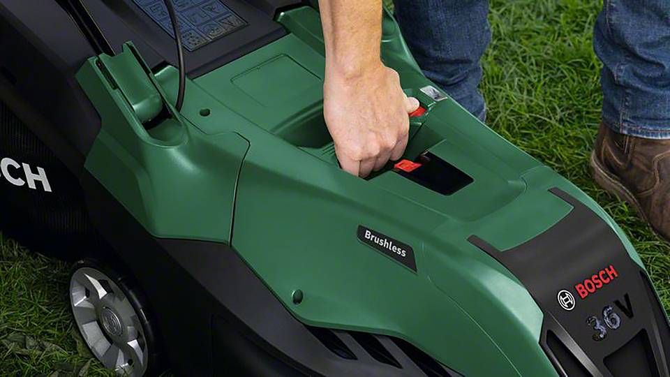 Une personne insère une batterie dans une tondeuse à gazon verte Bosch. Pelouse en arrière-plan.
