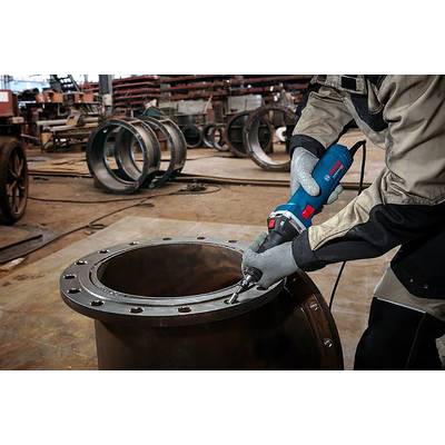 Une personne ponce les bords d'un grand tube métallique à l'aide d'un outil électrique dans un atelier. D'autres tronçons de tubes sont visibles en arrière-plan.