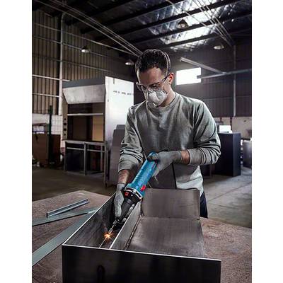 Un homme porte des lunettes de protection et un masque et soude du métal dans un atelier. Entouré d'équipements industriels et d'outils.