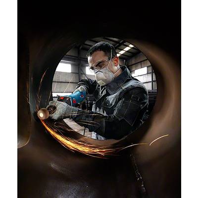 Une personne porte des vêtements de protection et meule du métal avec un outil électrique. Des étincelles volent pendant le travail dans un atelier.