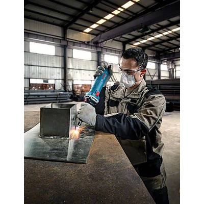 Un homme en tenue de protection soude du métal dans un grand atelier. Des étincelles volent tandis qu'il utilise un outil sur un cube métallique.