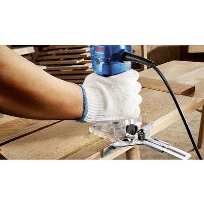 Une personne effectue un travail précis du bois avec une fraiseuse électrique bleue sur une table, produisant des copeaux de sciure.