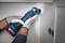 Une personne porte des gants et utilise un outil électrique pour découper un trou dans une paroi d'armoire.