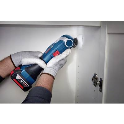 Une personne porte des gants de protection et utilise un outil multifonction sans fil pour couper à l'intérieur d'un placard de cuisine.