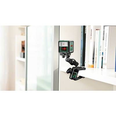Un télémètre laser est fixé à une étagère, projetant une croix de visée rouge sur le mur opposé. Des livres sont visibles en arrière-plan.