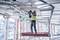 Un ouvrier en tenue de protection se tient sur un échafaudage et effectue des travaux d'installation au plafond dans un bâtiment en cours de construction.