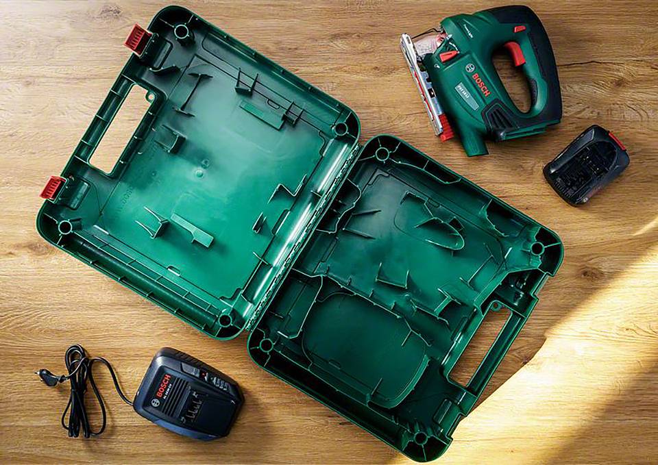 Ensemble de visseuse sans fil avec mallette verte, chargeur et batterie posés sur une table en bois. Appareil en haut à droite, mallette ouverte au centre.