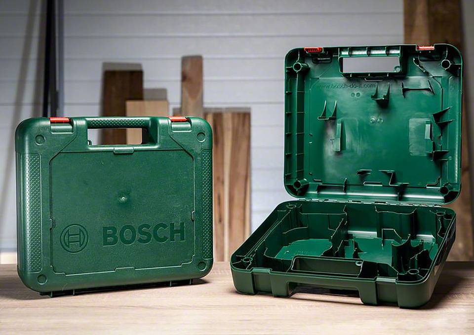 Coffret à outils Bosch vert ; un coffret fermé, l'autre ouvert et vide, posé sur une table en bois avec un arrière-plan d'atelier.
