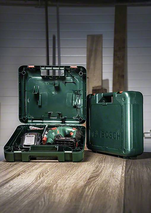 Valise Bosch verte ouverte et fermée sur une table en bois. À l'intérieur, un ensemble de visseuse sans fil avec accessoires est visible. Arrière-plan flou.