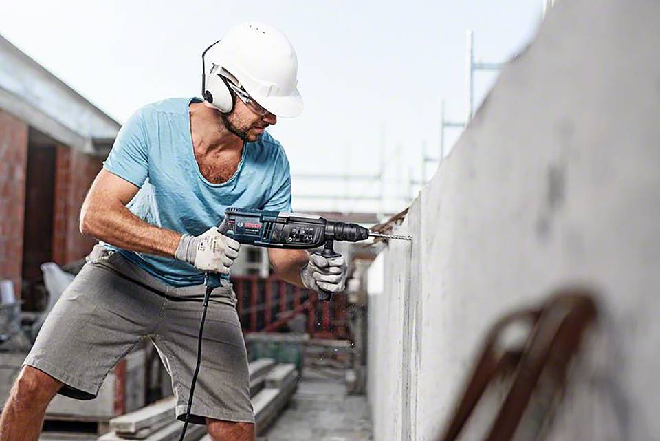Un ouvrier porte un casque et des lunettes de protection et utilise une perceuse électrique pour percer un trou dans un mur en béton.