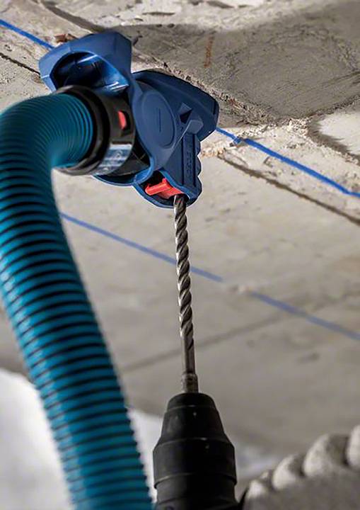'Perceuse en action sur un plafond en béton, avec un embout d'aspirateur bleu qui élimine la poussière.'