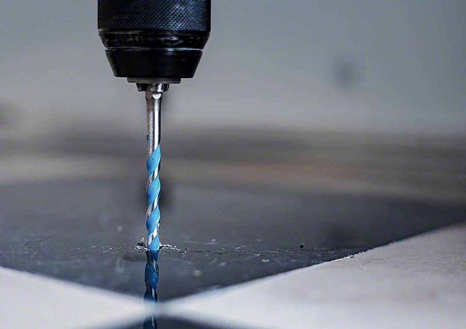 Plan rapproché d'une mèche en train de percer un trou dans une surface lisse et noire. La mèche a un revêtement spiralé bleu.