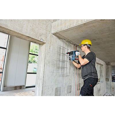 Un ouvrier portant un casque jaune fore un mur en béton avec une perceuse électrique sur un chantier de construction.