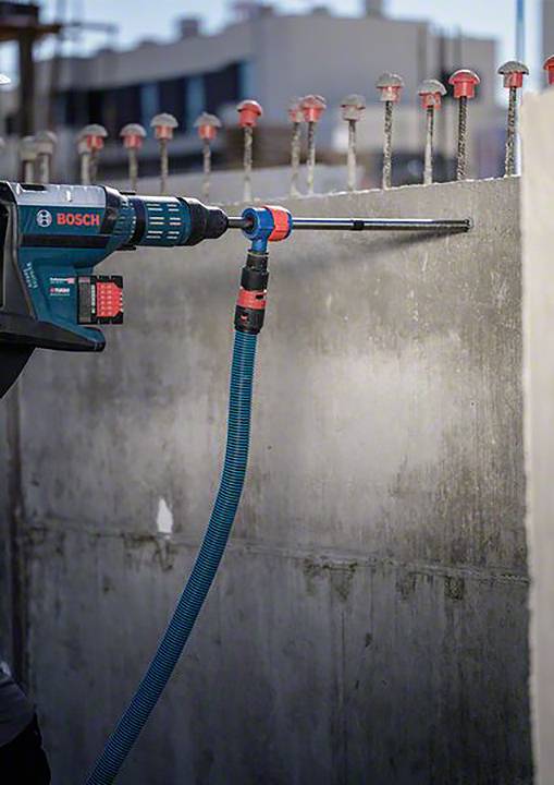 Un perceuse Bosch fore un trou dans un mur en béton sur un chantier de construction. Des renforts en acier sont visibles en arrière-plan.