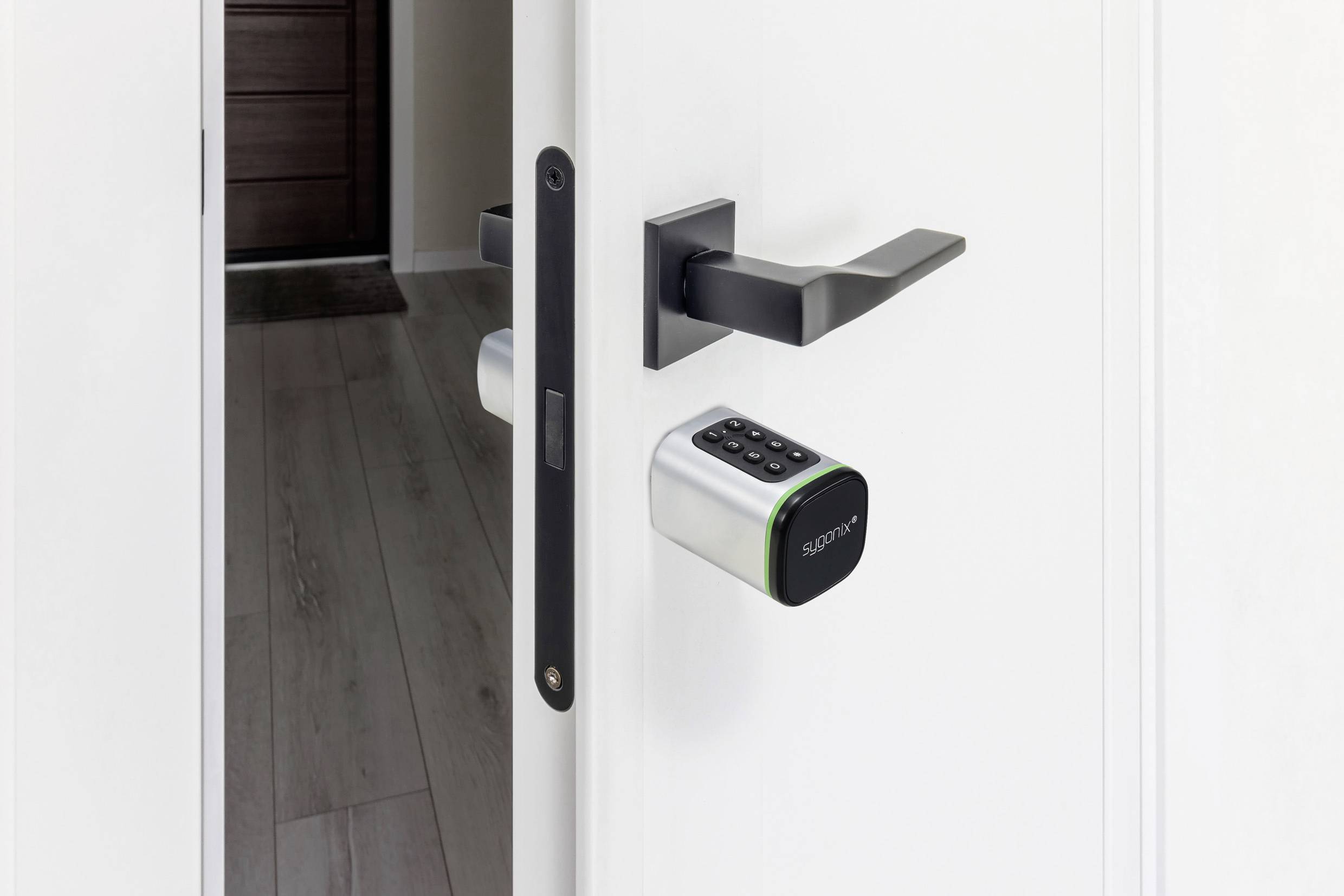 Porte blanche avec une serrure connectée affichant un pavé numérique. La porte est légèrement entrouverte, laissant apercevoir une partie d'un couloir en arrière-plan.