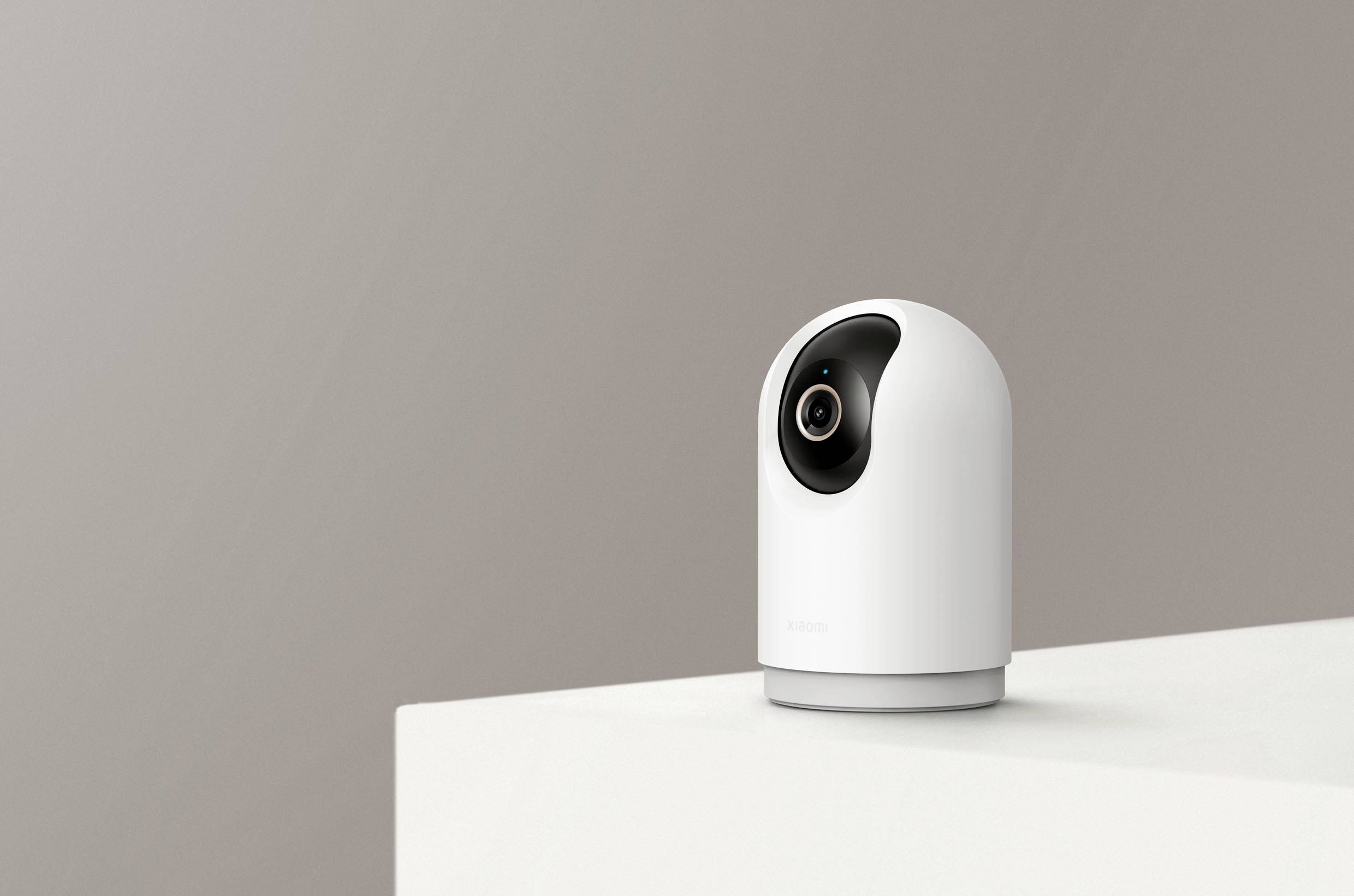 Une caméra de sécurité blanche est installée sur un socle blanc devant un fond gris ; un design moderne et minimaliste.