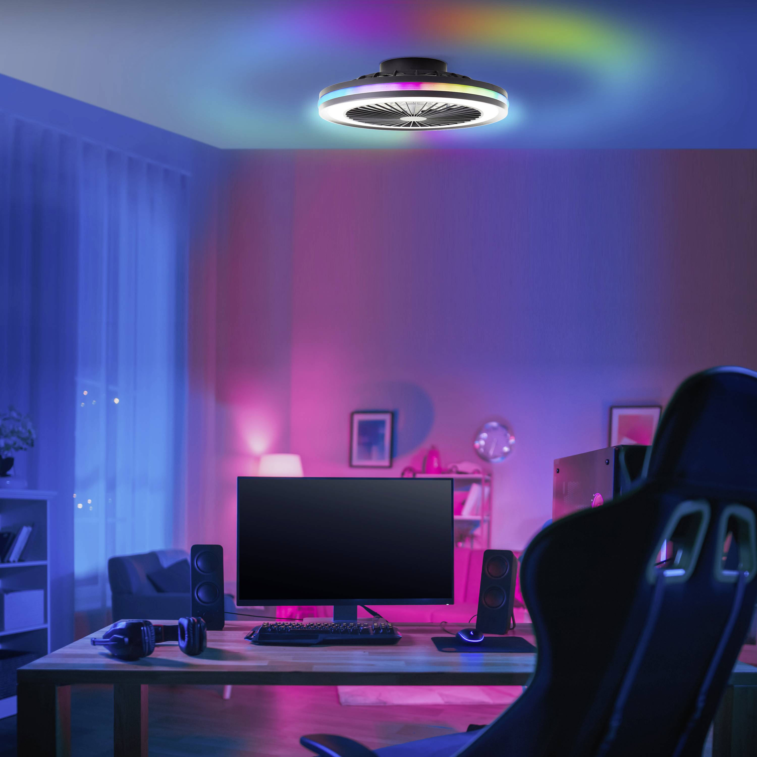 Un bureau moderne avec un ordinateur et des accessoires de gaming dans une pièce à l'éclairage d'ambiance. Des lumières colorées au plafond.