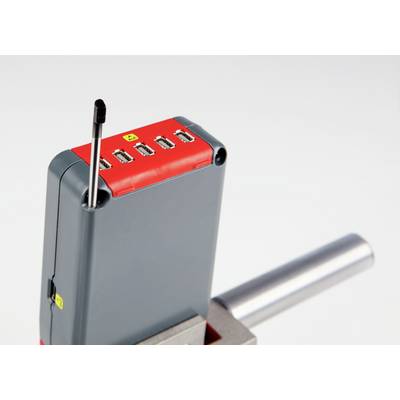 Un appareil gris avec un dessus rouge et quatre ports USB. Une petite antenne est déployée. Il est posé sur une surface métallique.