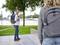 Un homme avec un sac à dos regarde en souriant derrière lui, alors qu'il se promène dans un parc surplombant une rivière. Une personne floue se trouve au premier plan.