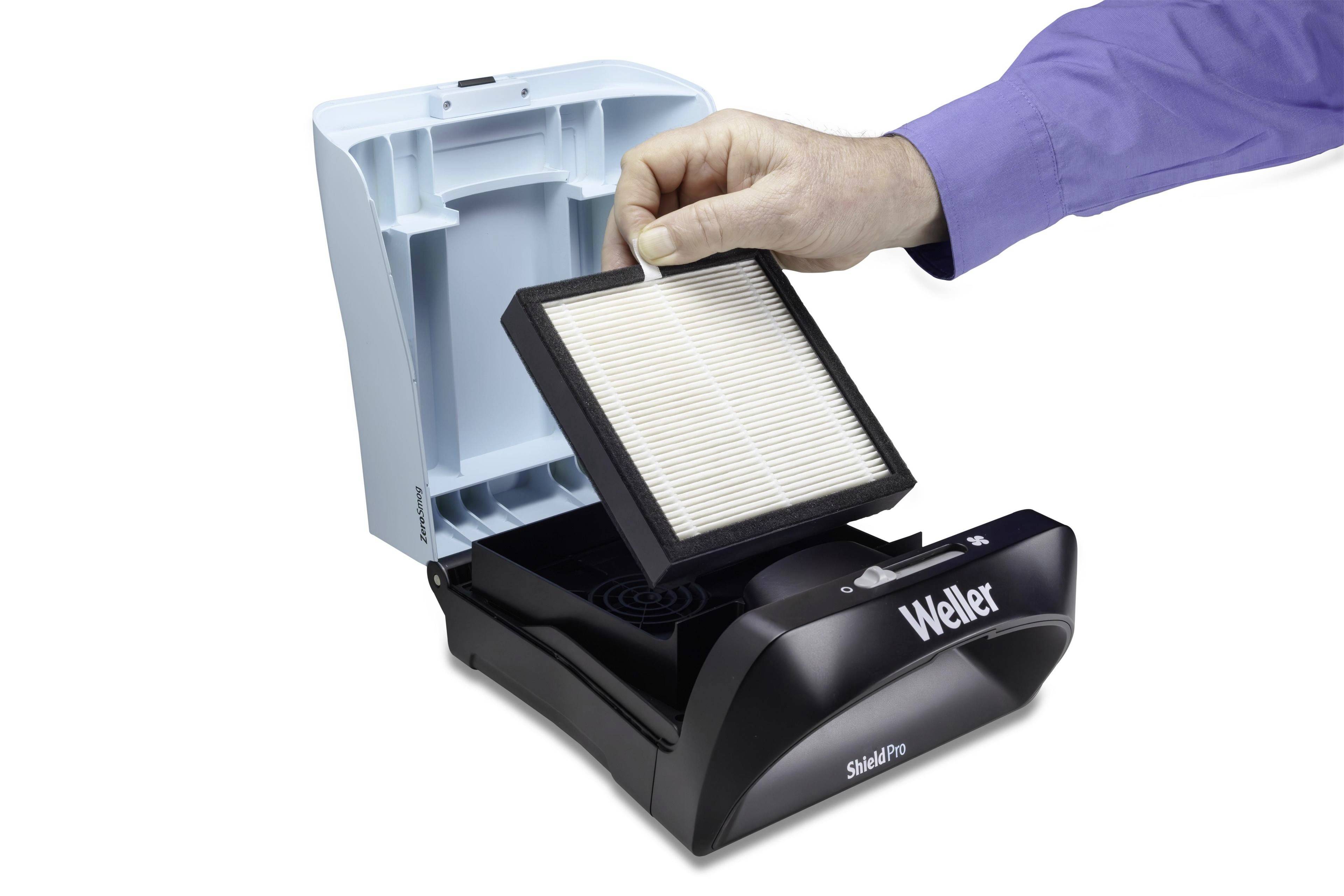 Une main change le filtre d'un purificateur d'air Weller. L'appareil est ouvert pour permettre le remplacement de l'élément filtrant.