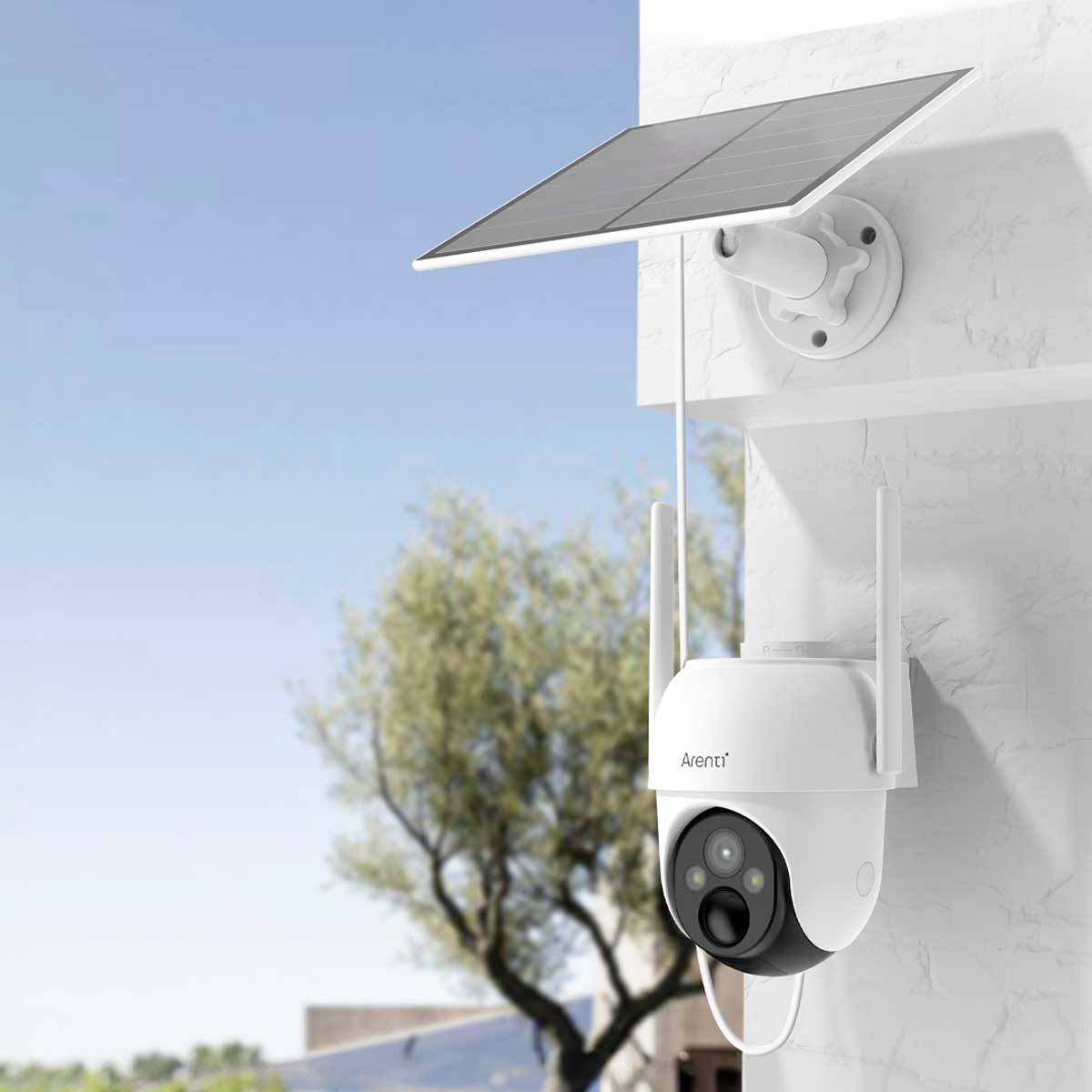 Caméra de surveillance montée sur un mur, alimentée par un panneau solaire. Des arbres flous sont visibles en arrière-plan.