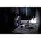 Une femme travaille sur un ordinateur portable la nuit pendant un orage. Une lampe éclaire la table. Des éclairs sont visibles à travers la fenêtre.
