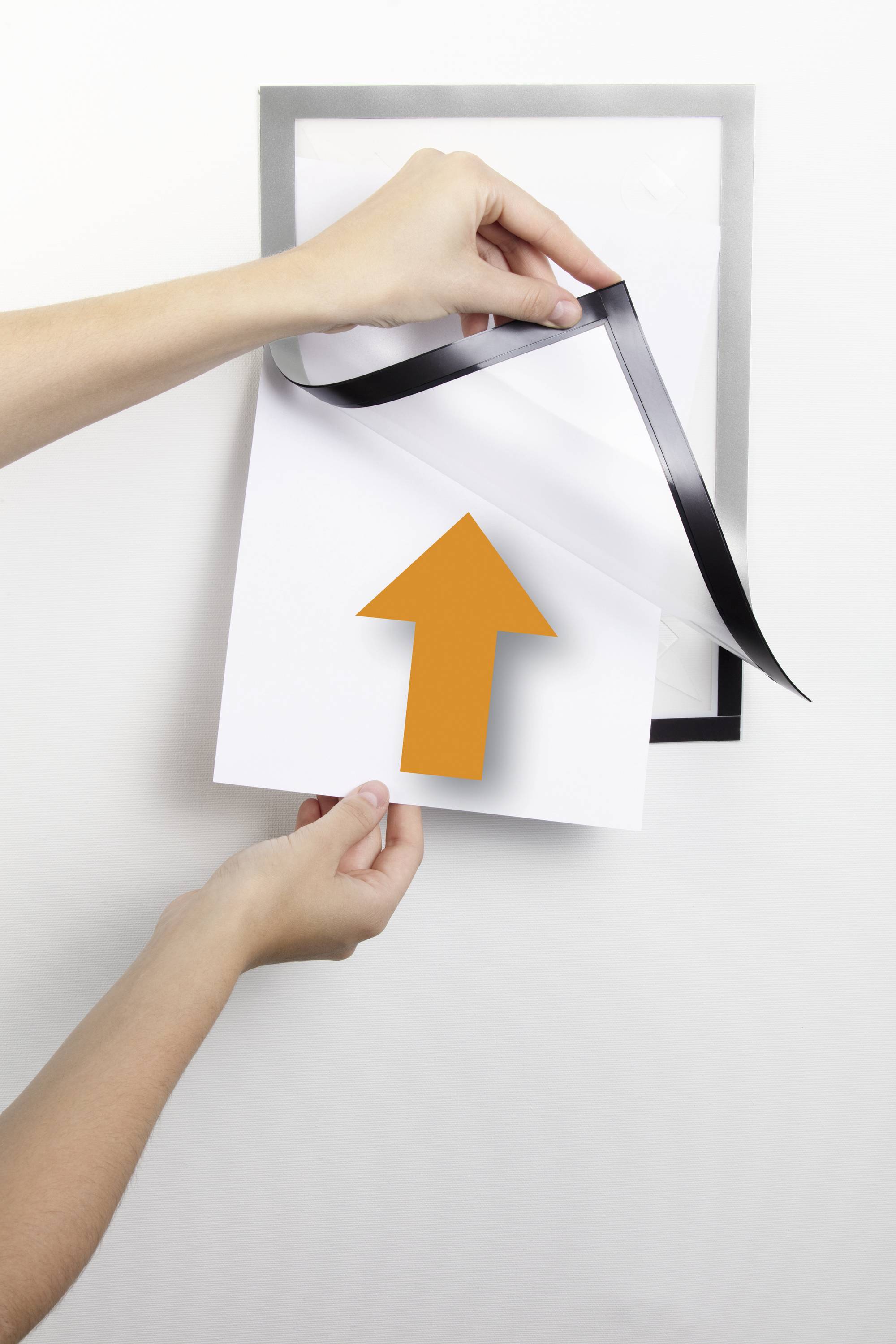 Une main retire une feuille avec un bord noir et une flèche orange d'un compartiment transparent fixé au mur.