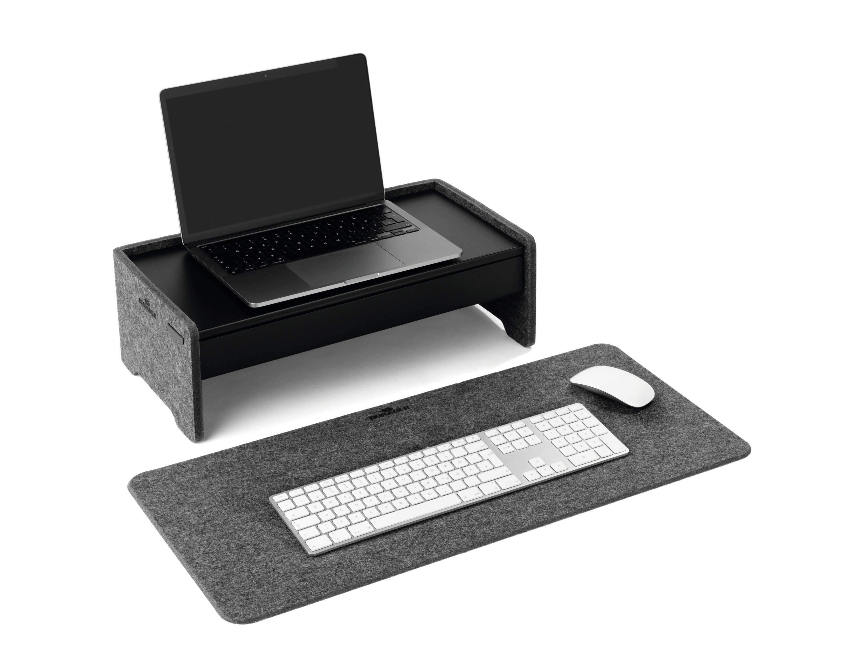 Ordinateur portable posé sur un support gris surélevé, avec un clavier et une souris sur un tapis en feutre gris en dessous. Design moderne et minimaliste.