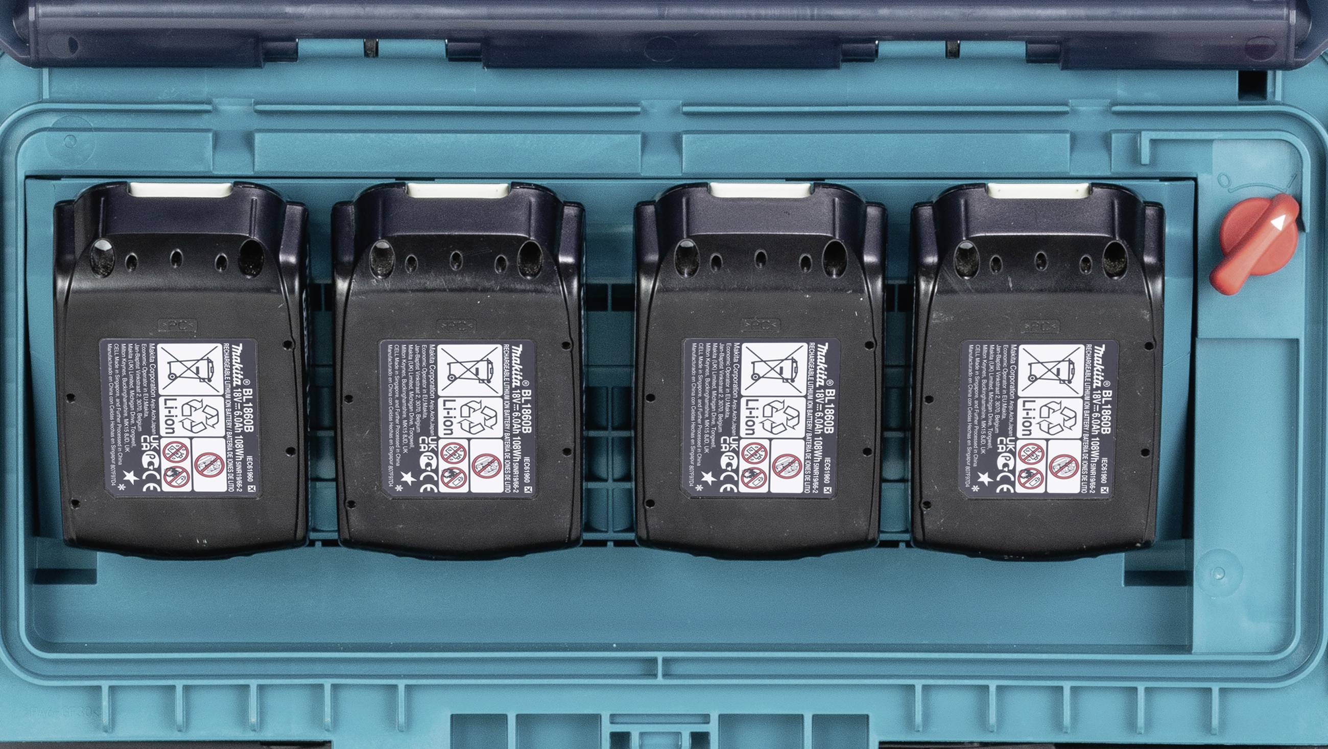 Quatre batteries noires sont alignées côte à côte dans un coffret bleu. Des symboles d'avertissement sont visibles sur chaque batterie.