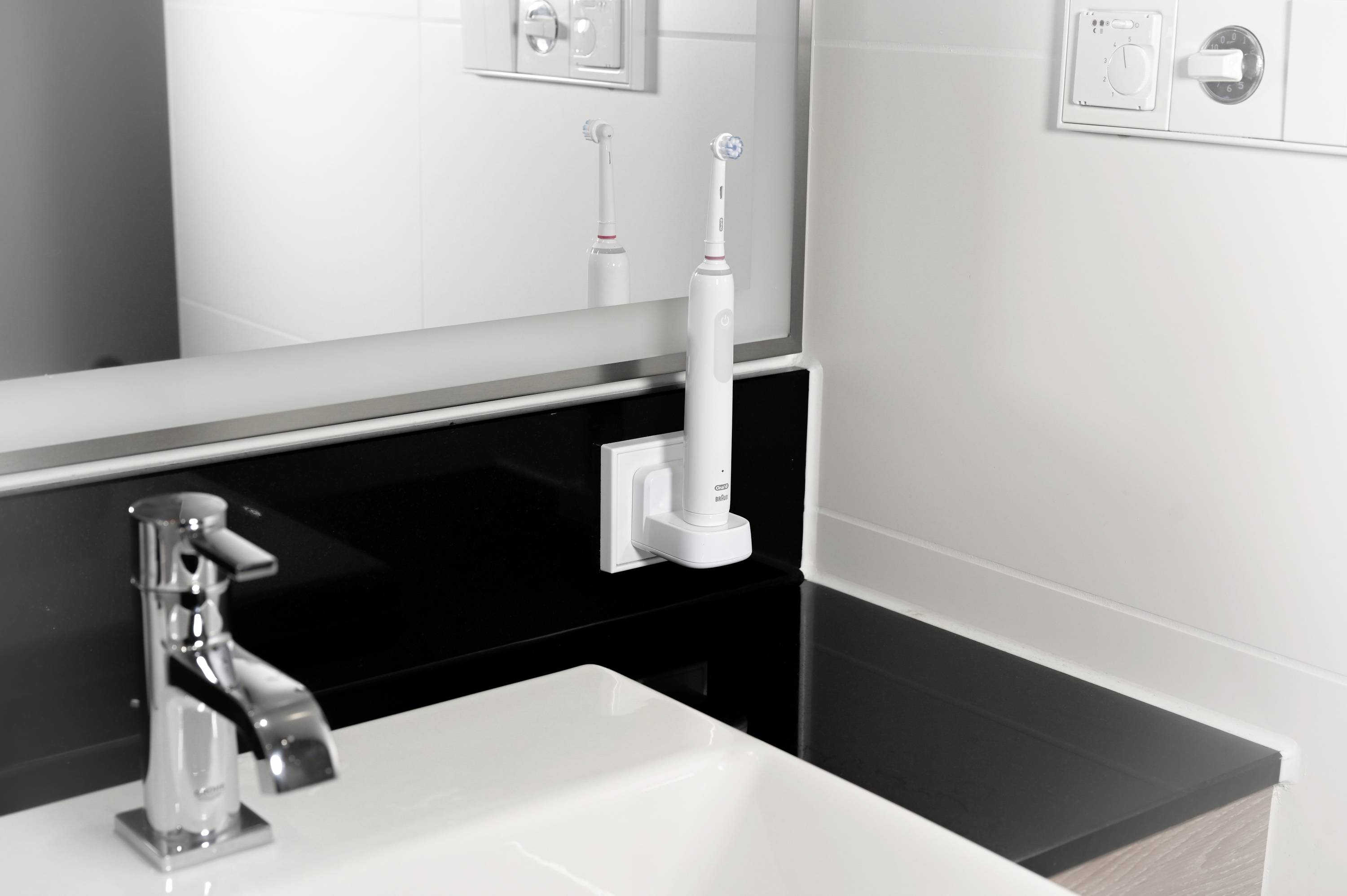 Brosse à dents électrique sur sa station de charge à côté du lavabo, un miroir en arrière-plan reflétant la brosse.