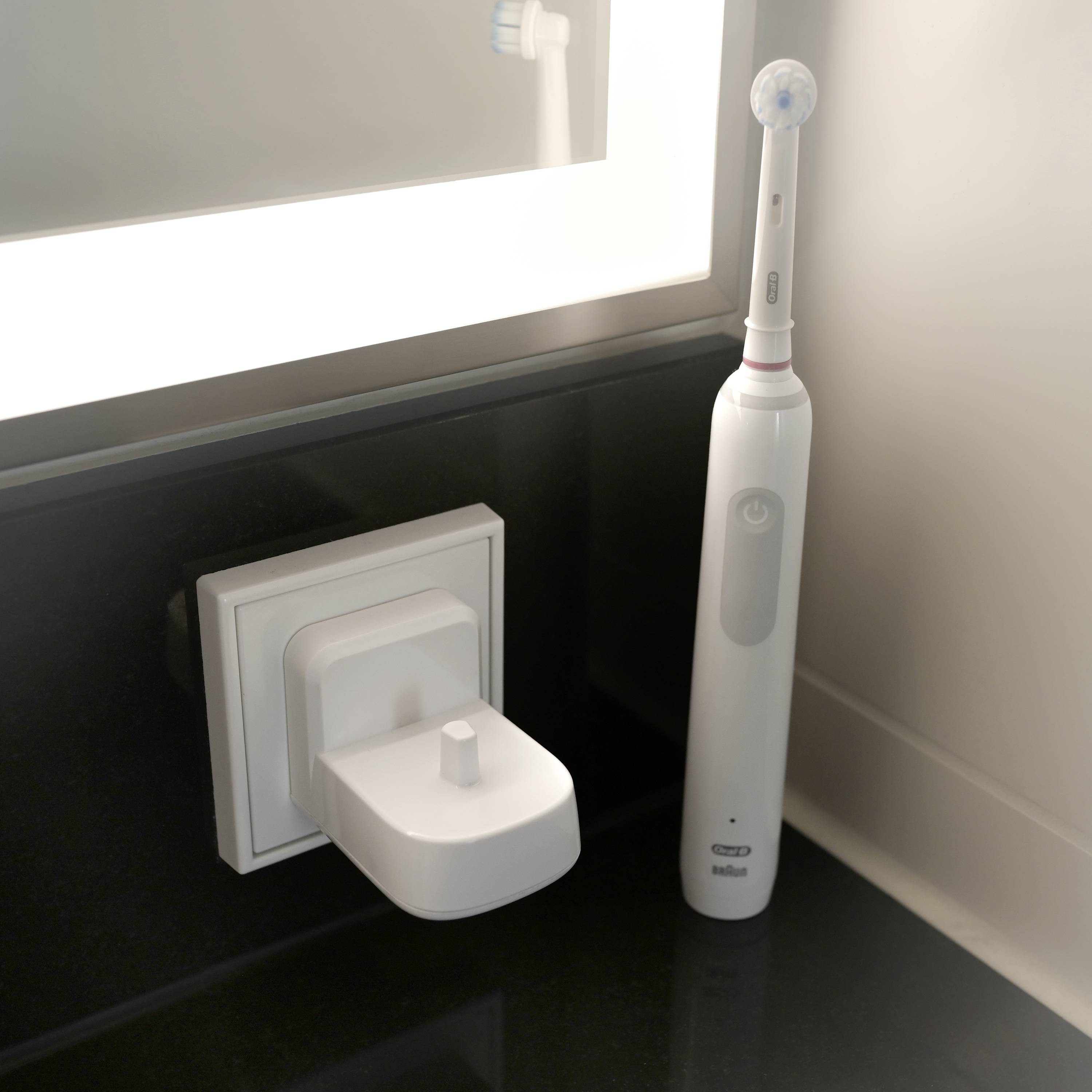 Une brosse à dents électrique est posée dans sa station de charge sur un lavabo, à côté d'un miroir éclairé.