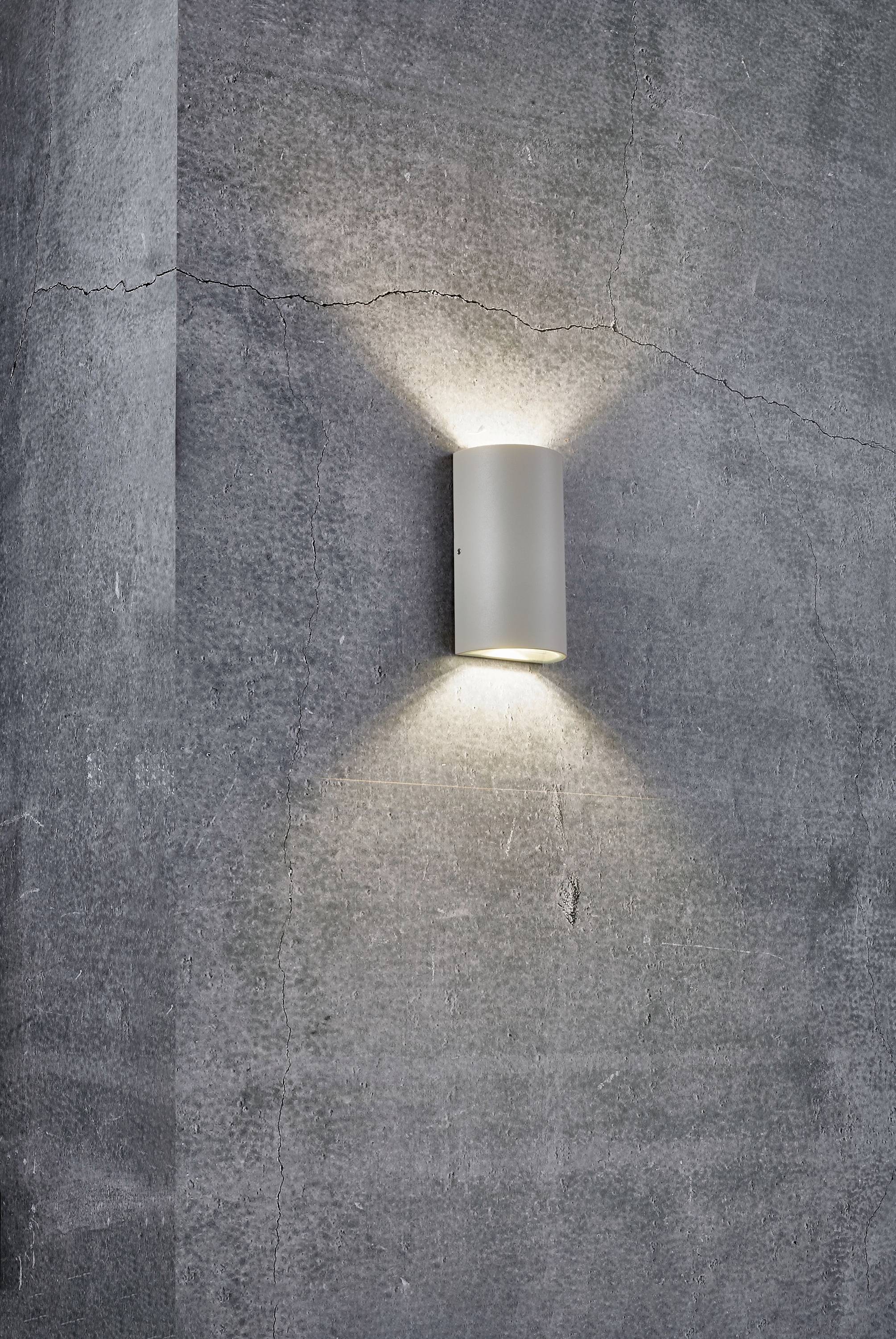 Un luminaire mural moderne qui projette une lumière douce vers le haut et le bas sur un mur en béton gris.