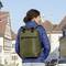 Un homme portant un anorak bleu et un sac à dos vert olive se tient devant des bâtiments historiques dans un environnement urbain.