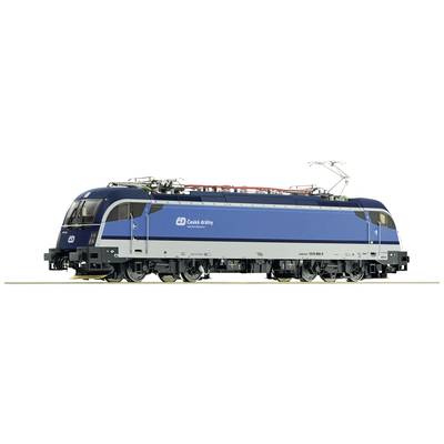 Un train bleu des České dráhy est stationné sur des voies ferrées, avec des détails visibles tels que le pantographe et les roues, sur un fond blanc.