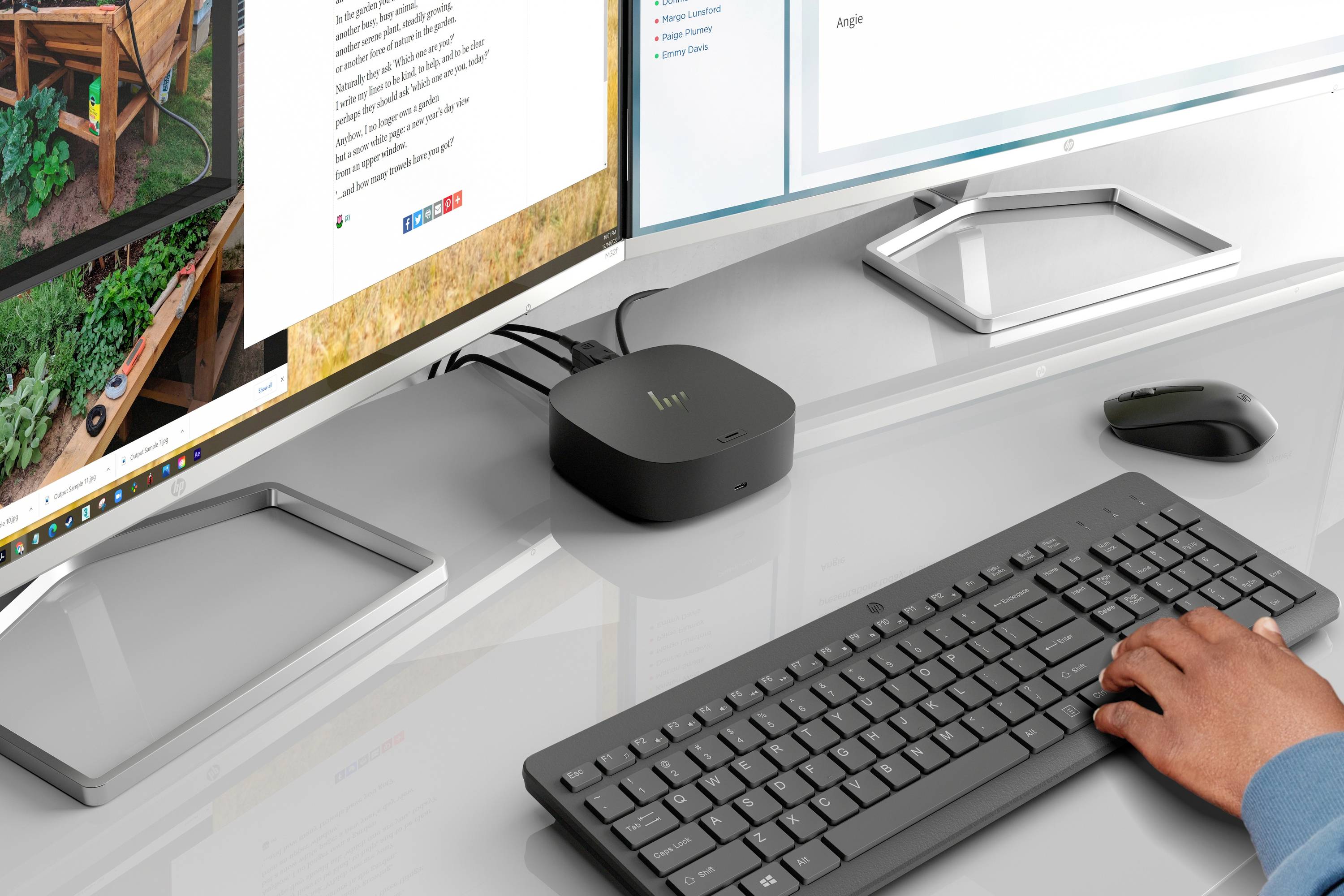 Une personne tape sur un clavier et une souris à un poste de travail moderne avec deux écrans. Un petit ordinateur noir est connecté.