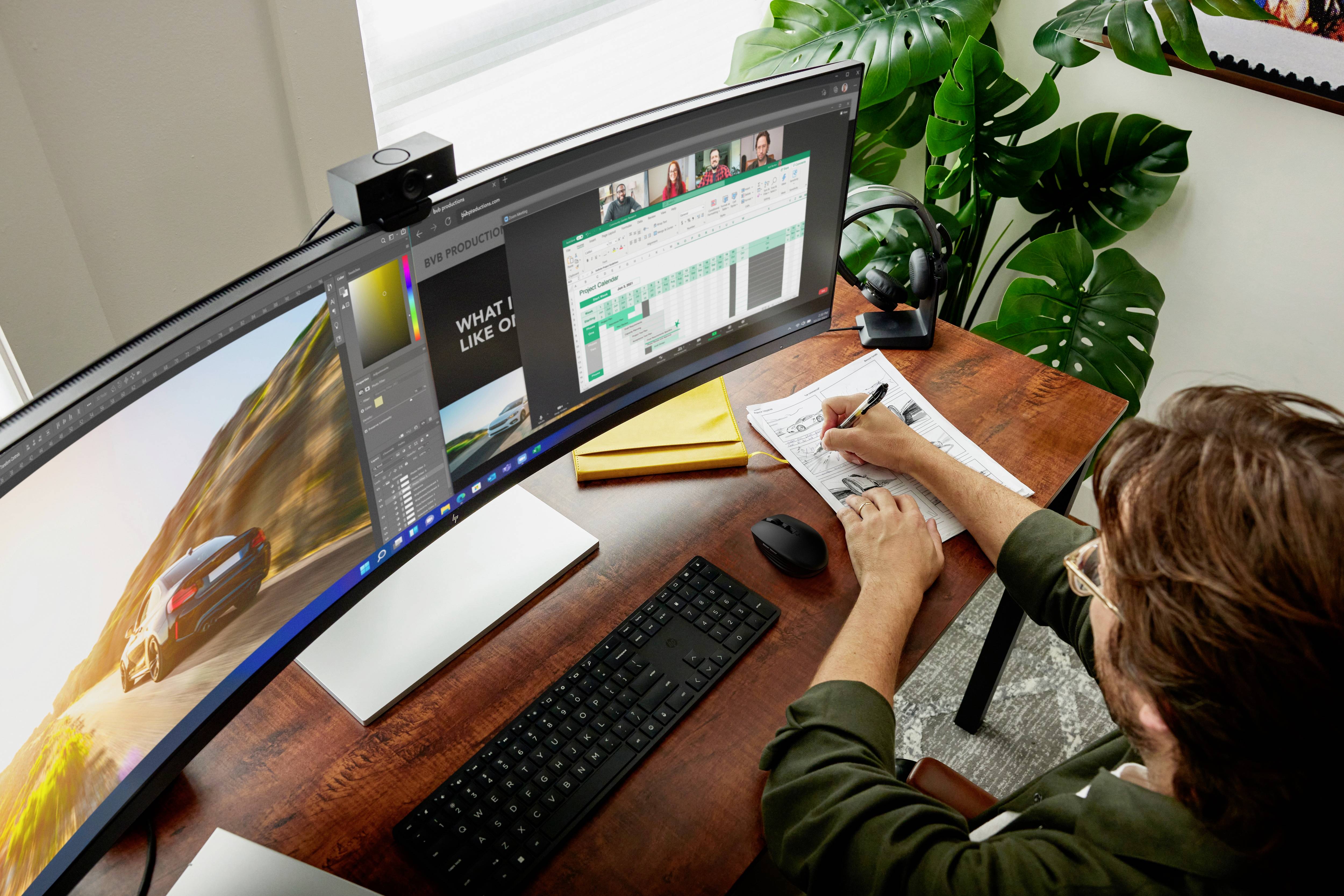 Une personne travaille à un bureau avec un grand écran incurvé, prenant des notes tandis que plusieurs fenêtres de programme sont ouvertes.