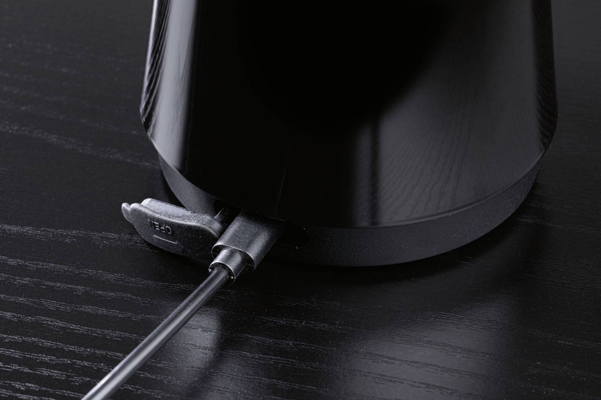 Un appareil électrique noir posé sur une table sombre, avec un câble d'alimentation branché à sa base.