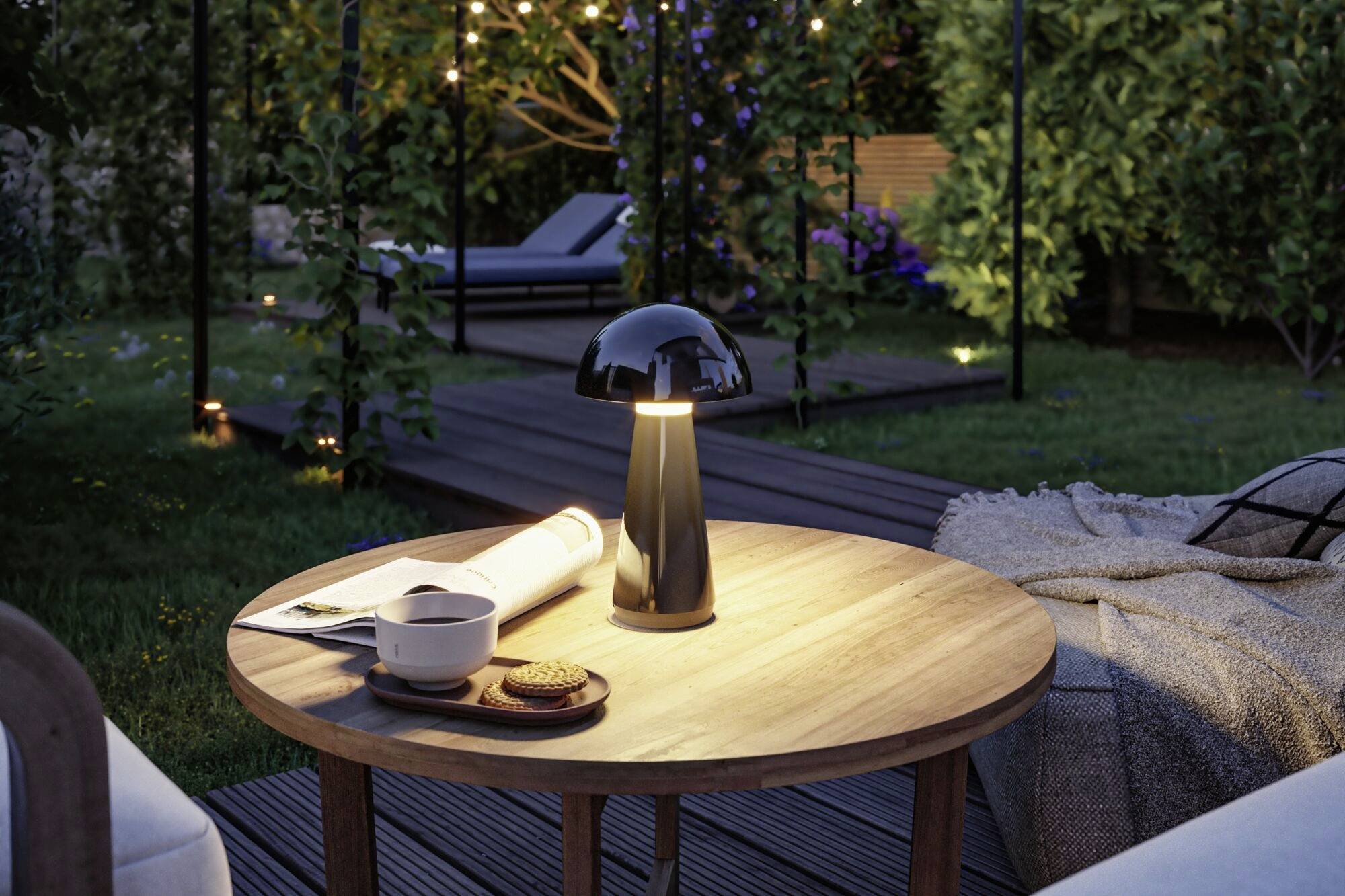 Une table ronde en bois dans le jardin avec une lampe, une tasse de café et un livre ouvert. À l'arrière-plan, un jardin éclairé.