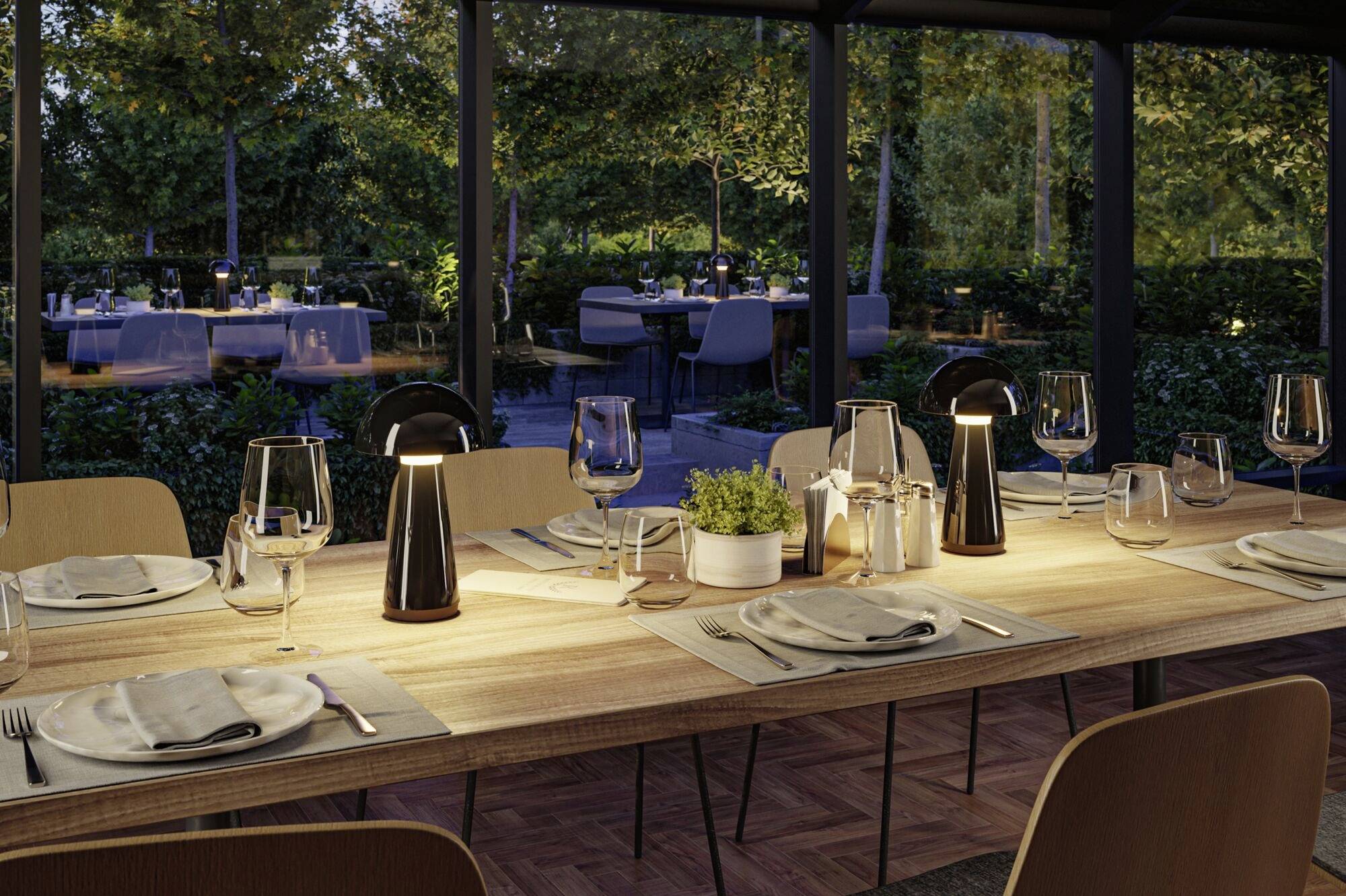 Une table élégamment dressée dans un restaurant, entourée de grandes fenêtres offrant une vue sur un jardin illuminé.