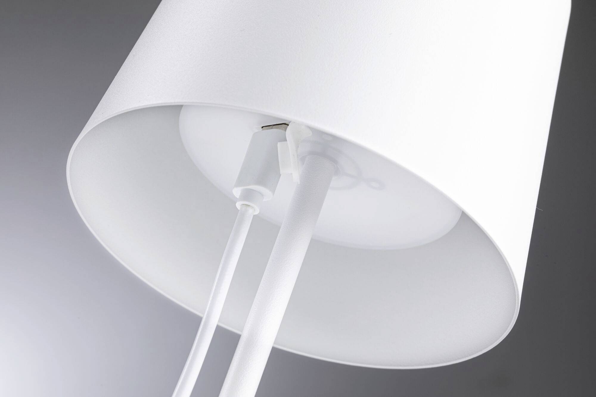Une lampe de table blanche avec un abat-jour rond et deux câbles sortant par le bas. Elle éclaire un environnement moderne et minimaliste.