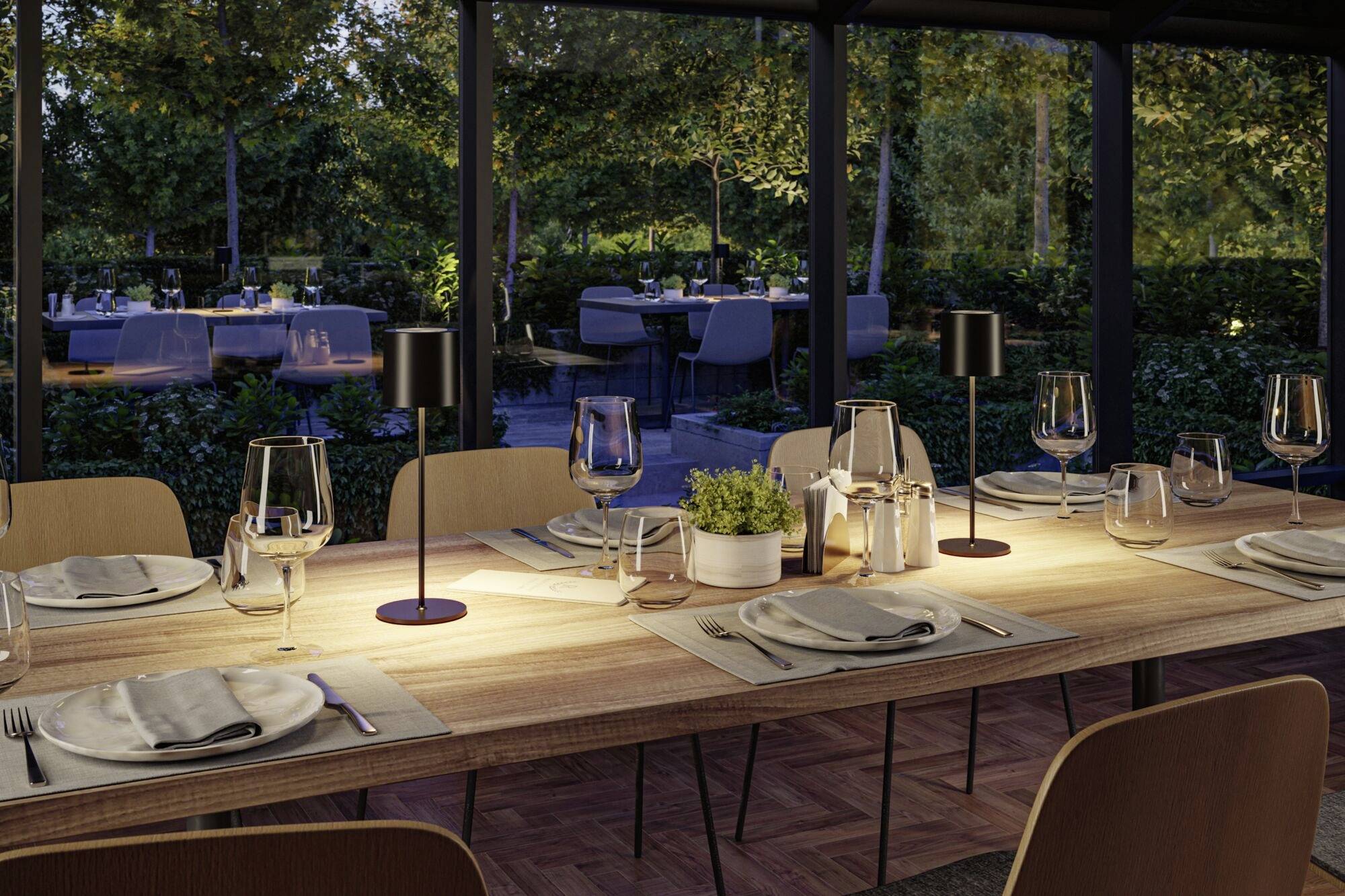 Une table dressée avec élégance en extérieur, avec des verres à vin et des assiettes, entourée d'arbres et d'autres tables de restaurant en arrière-plan.