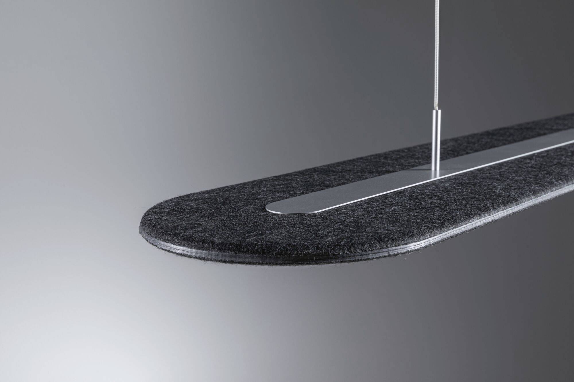Suspension design moderne en feutre gris, suspendue à un fin câble métallique devant un fond gris.