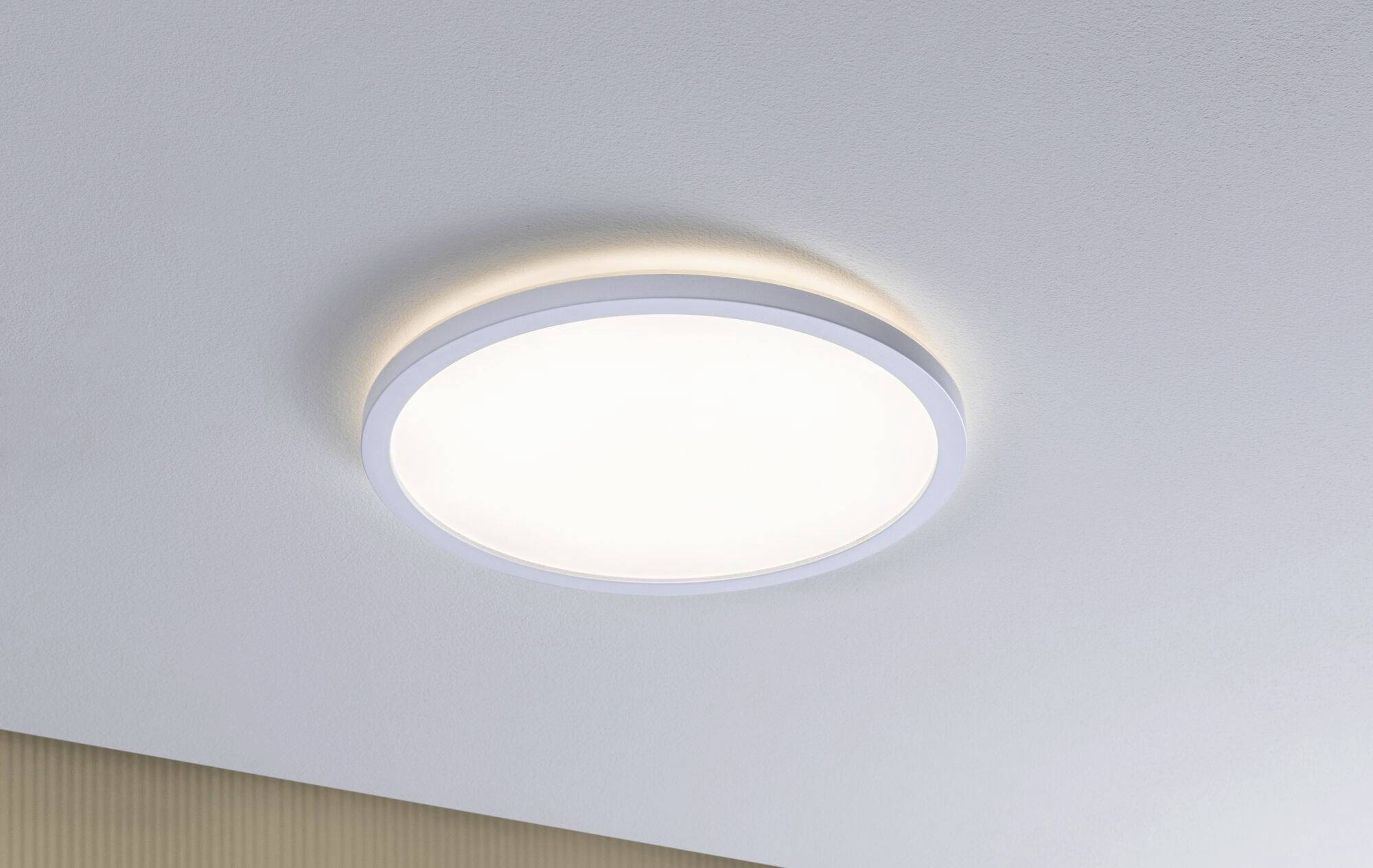 Une lampe de plafond ronde avec un éclairage LED lumineux est fixée à un plafond blanc et assure un éclairage uniforme dans la pièce.