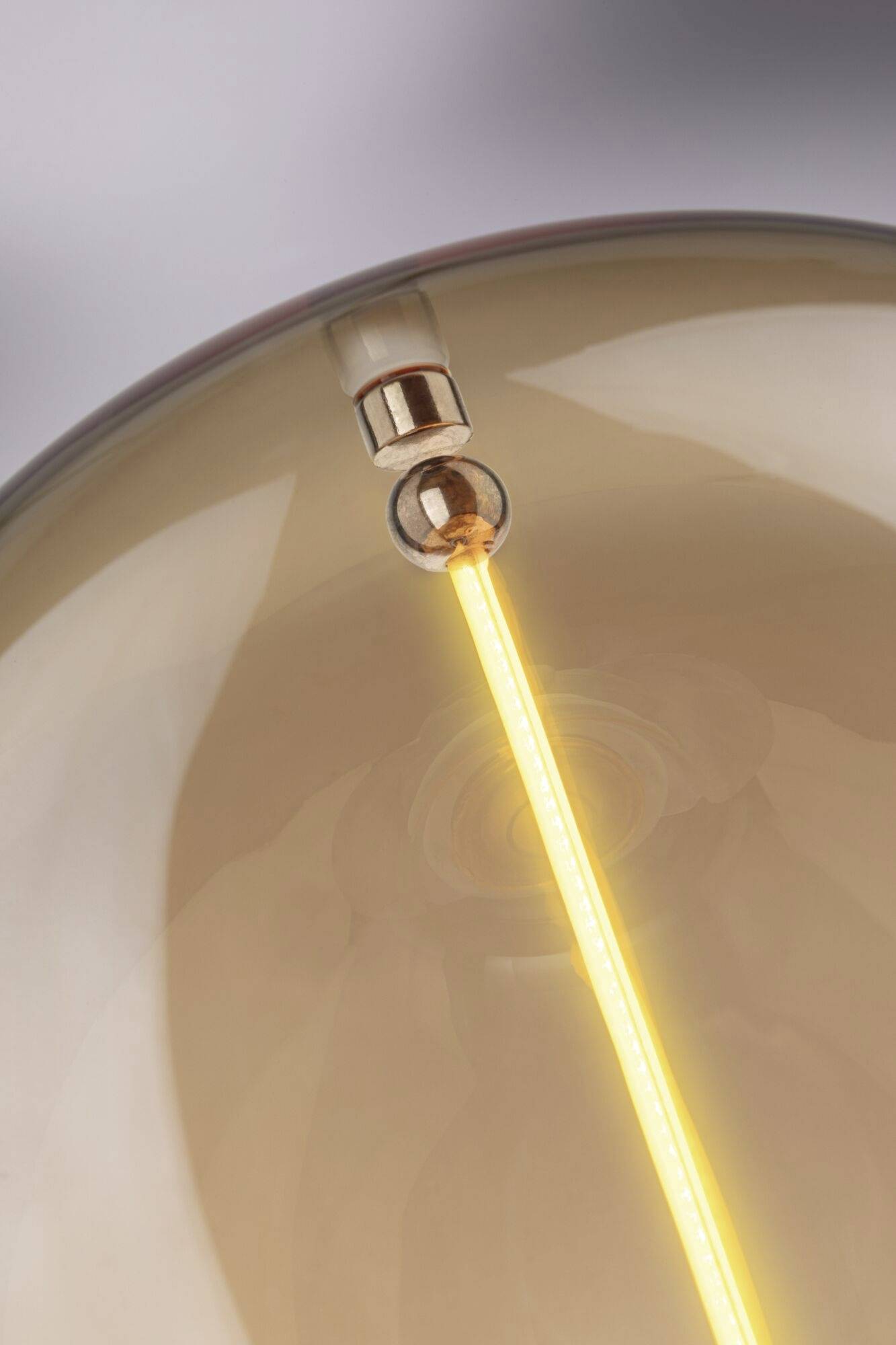 Gros plan d'une ampoule à lumière chaude avec un filament visible dans un espace doucement éclairé, créant une ambiance chaleureuse et intime.