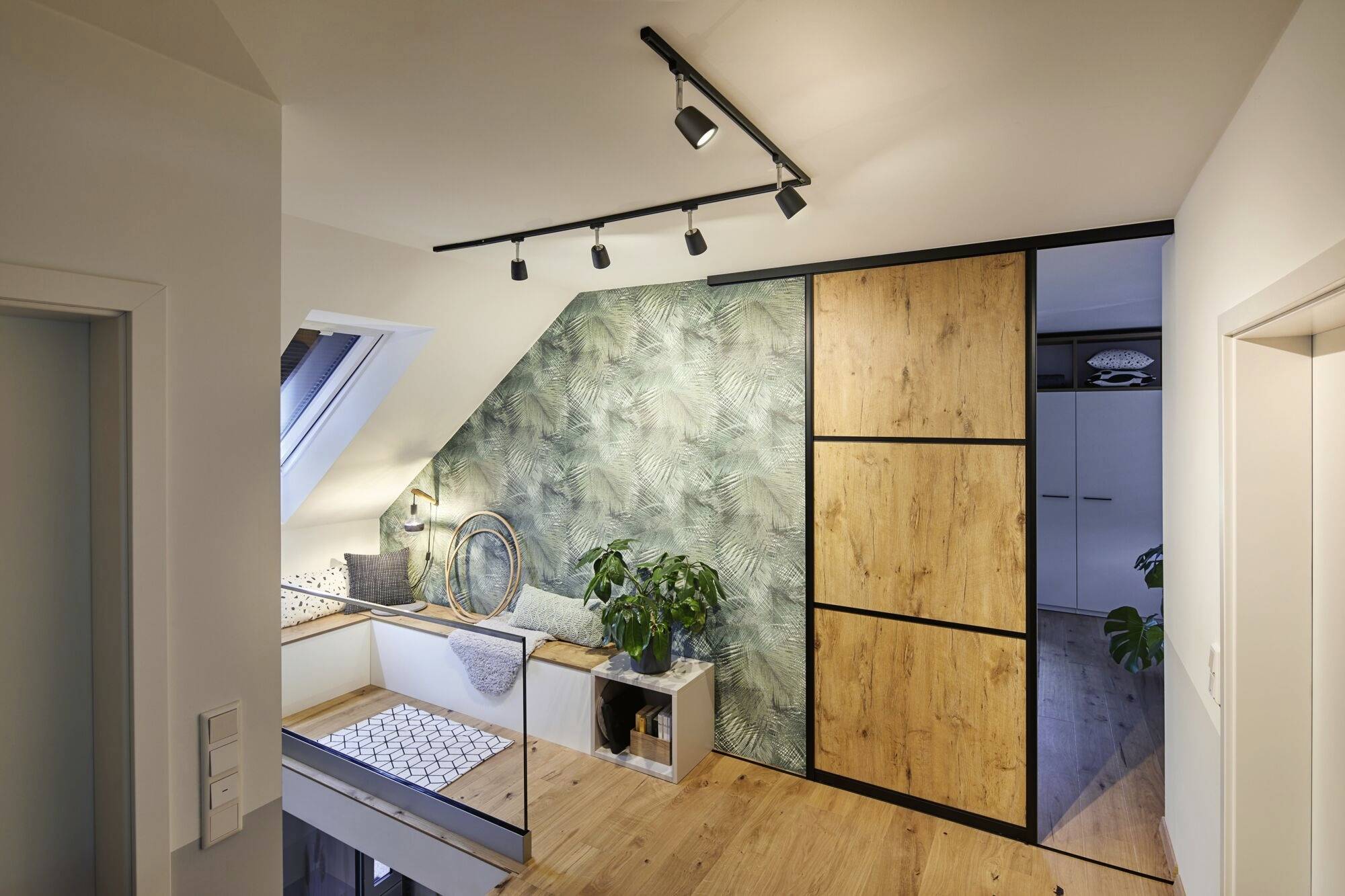 Chambre lumineuse, au design moderne, avec fenêtre de toit, plantes et touches de bois. Armoire en bois et papier peint à motifs de feuilles sur le mur de droite.