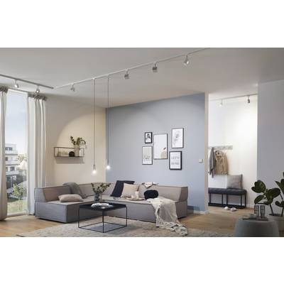 Un salon moderne avec un canapé d'angle, une table basse et un mur décoratif orné de cadres. La lumière du jour entre par la fenêtre.