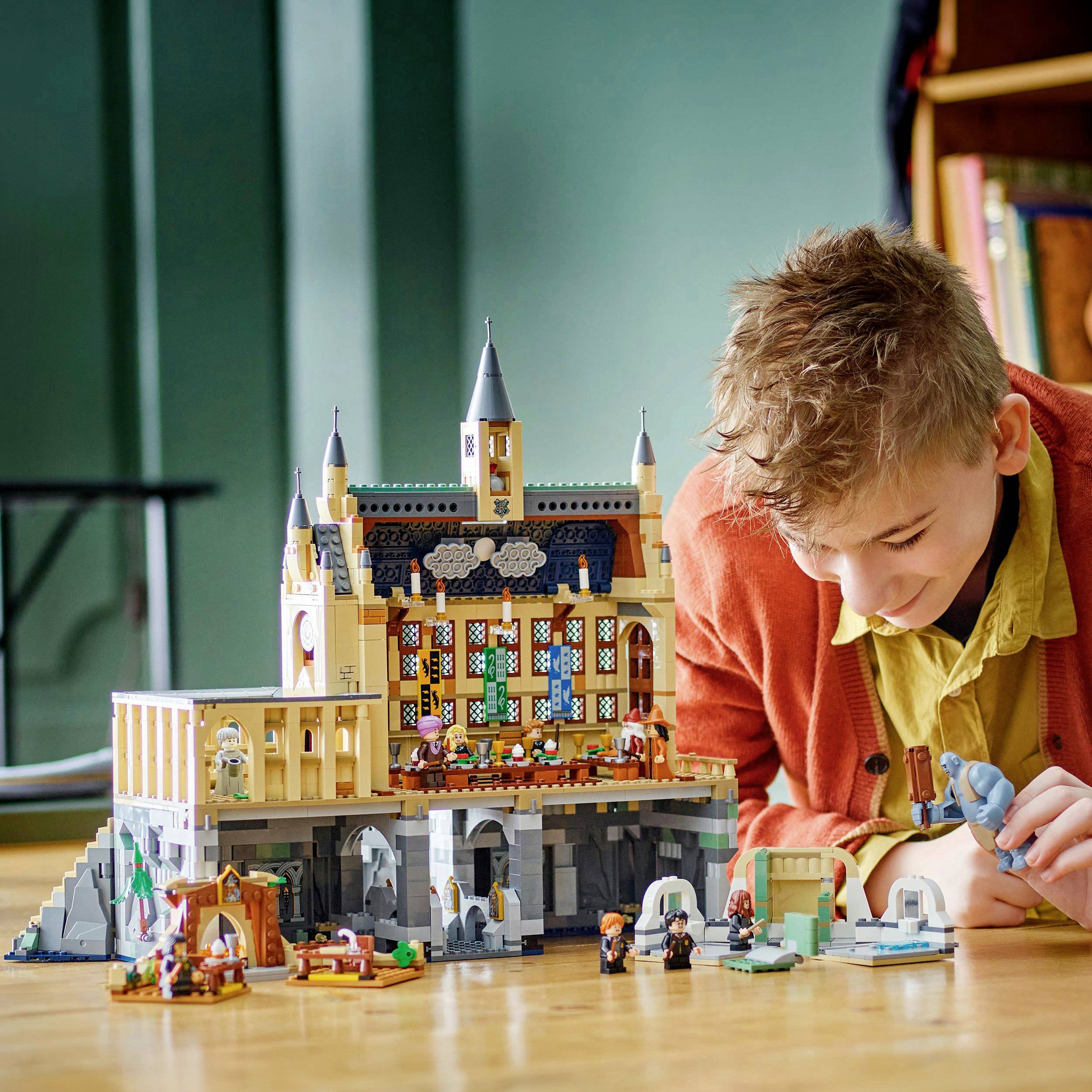 Un enfant joue avec un grand modèle de château détaillé, concentré sur les figurines qu'il dispose sur une table.