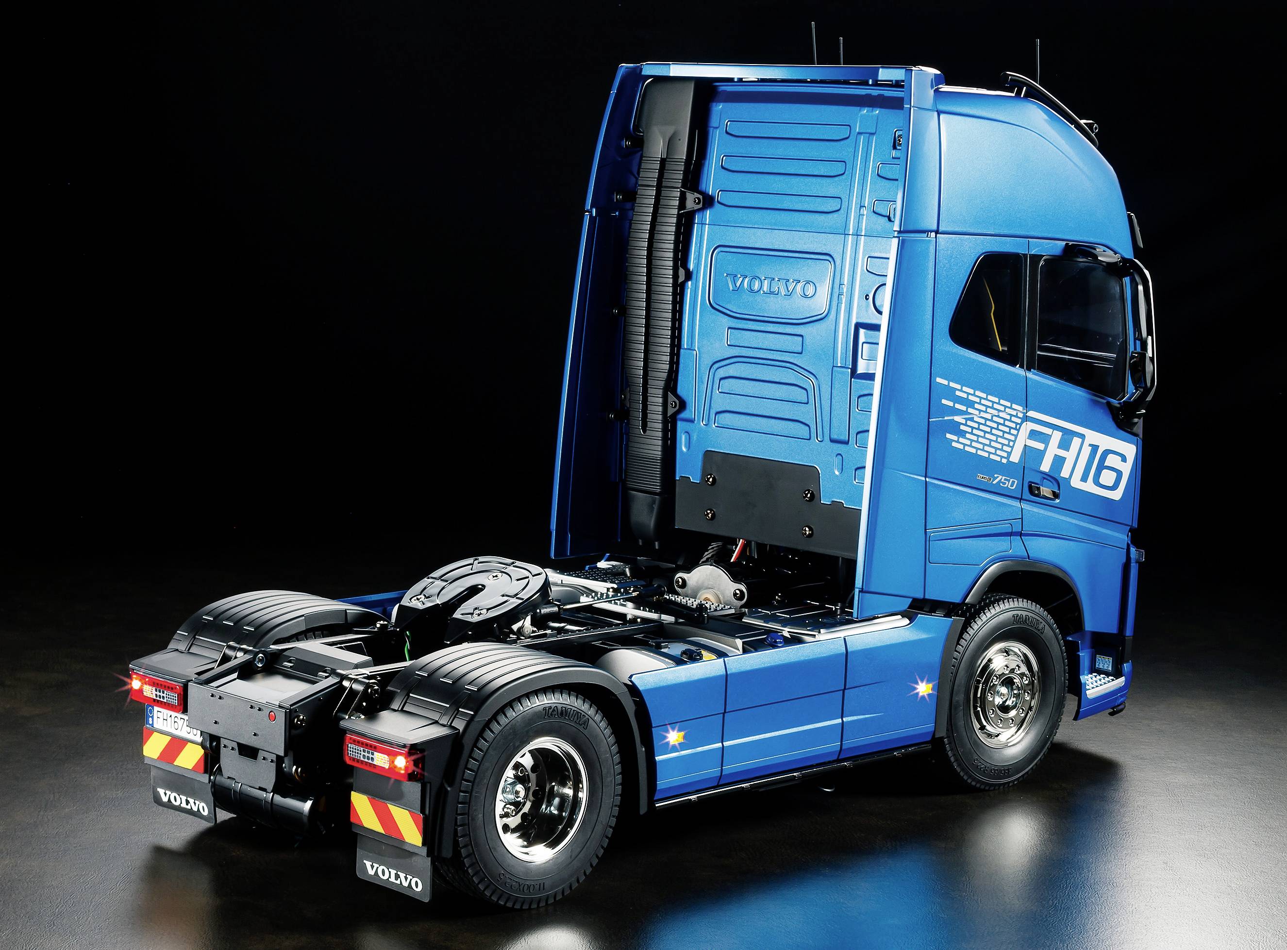 Un camion bleu sans remorque sur un fond sombre, photographié de côté par l'arrière, avec une surface de chargement vide et l'inscription 'FH16'.